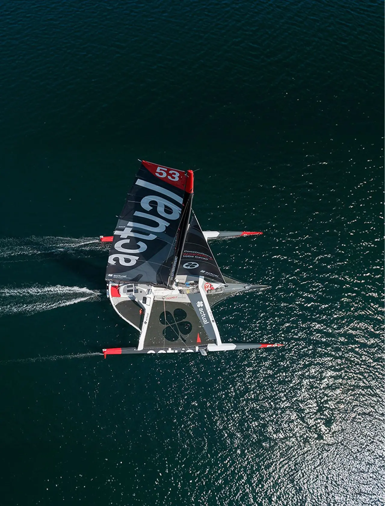 Vue aérienne du trimaran géant Ultim Actual naviguant en pleine mer.