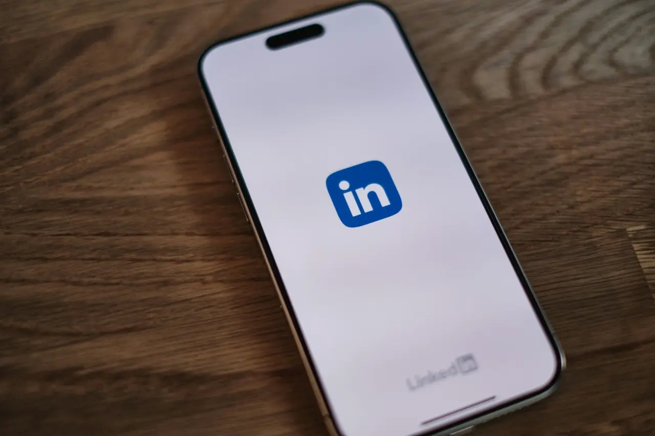 Un smartphone posé sur un bureau en bois affiche le logo du réseau professionnel LinkedIn.