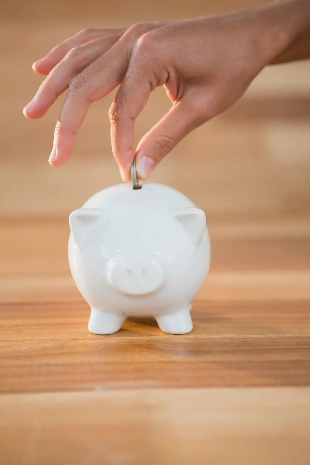 Une main dépose une pièce de monnaie dans une tirelire en forme de cochon pour illustrer le Compte Épargne Temps.