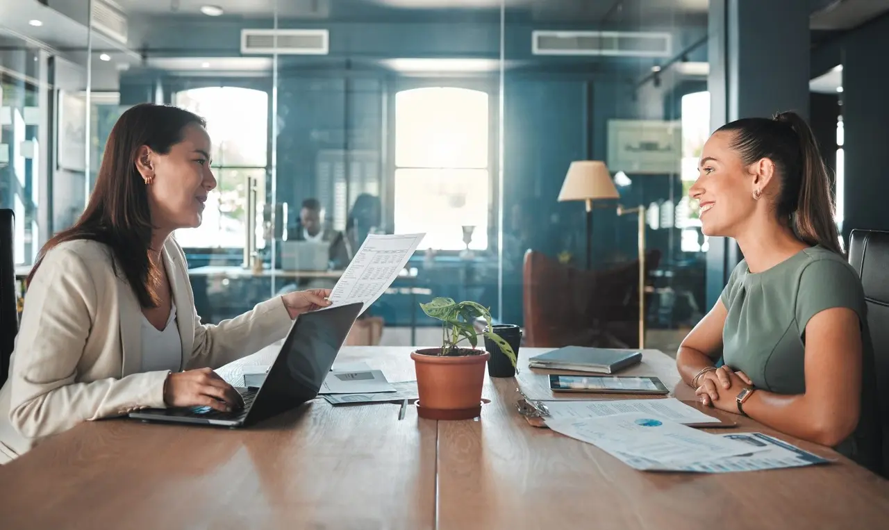 Une candidate et une recruteuse échangent avec le sourire lors d'un entretien d'embauche dans un bureau.