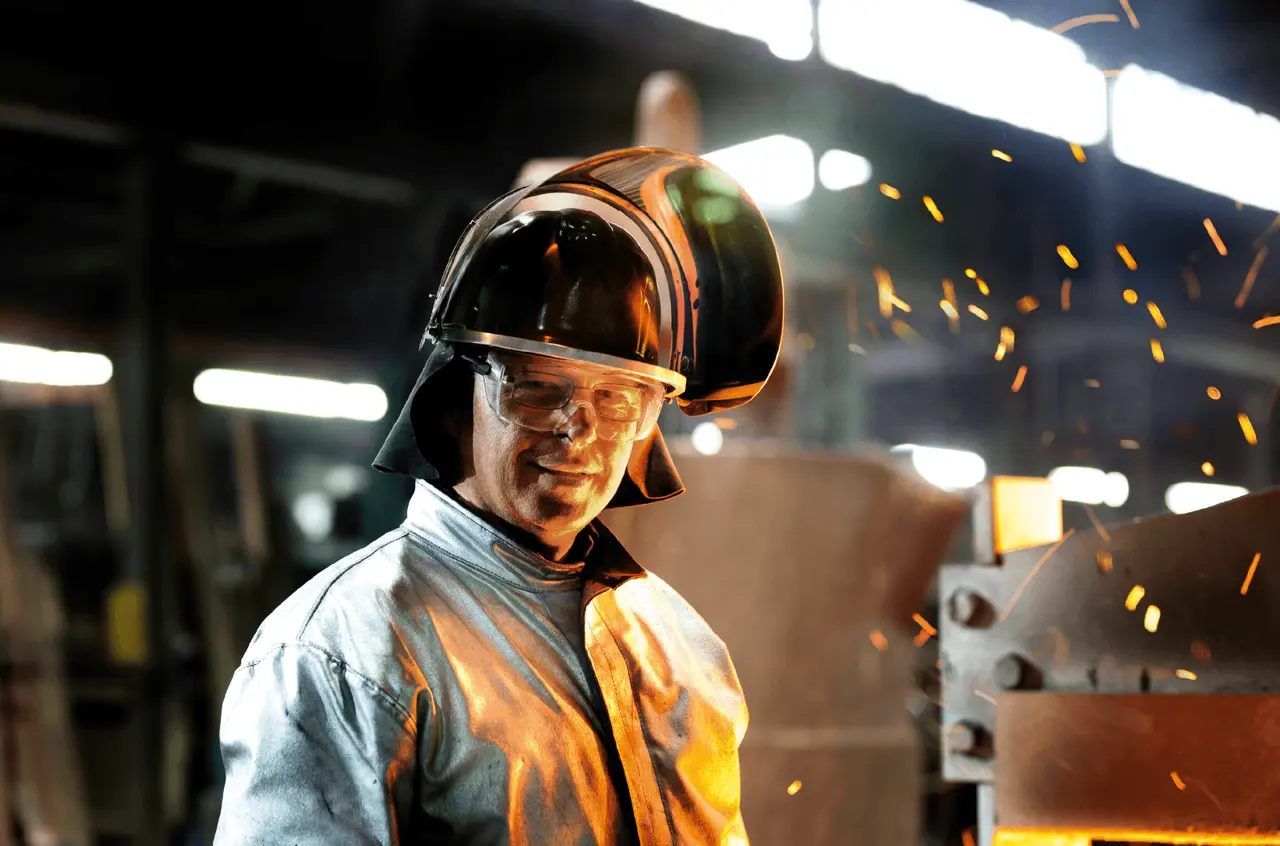 Un métallurgiste senior souriant en tenue de sécurité dans un atelier industriel.