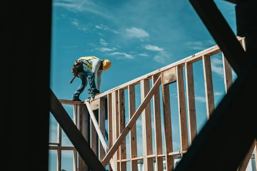 Un charpentier équipé d'un casque travaille sur l'ossature en bois d'un bâtiment en construction.
