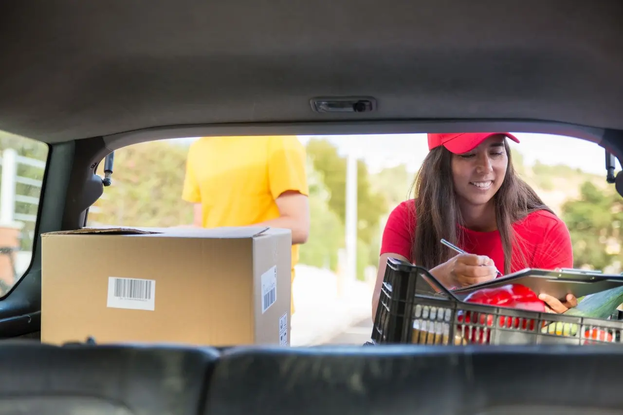 Une étudiante travaillant dans la livraison vérifie des colis et des légumes dans le coffre d'une voiture.