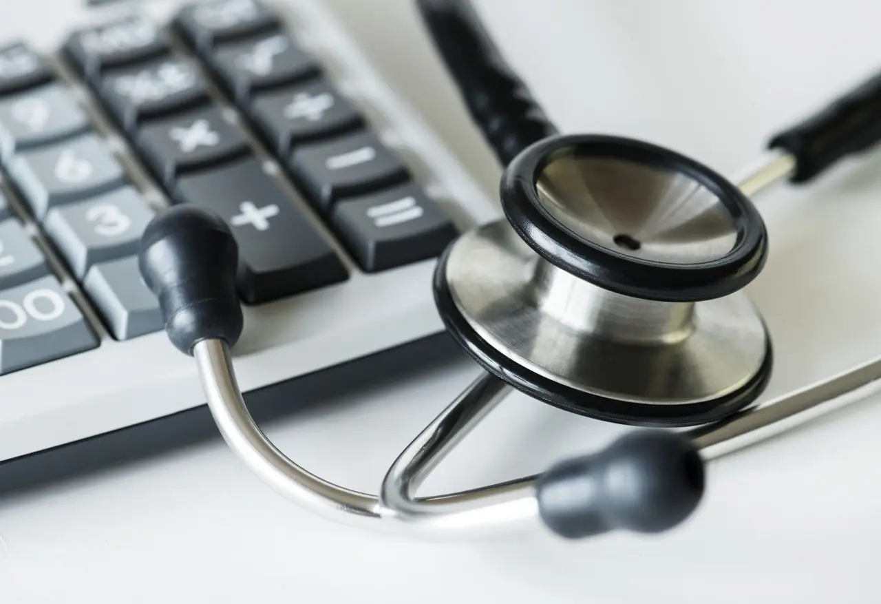 Un stéthoscope noir et argenté posé à côté d'une calculatrice de bureau.