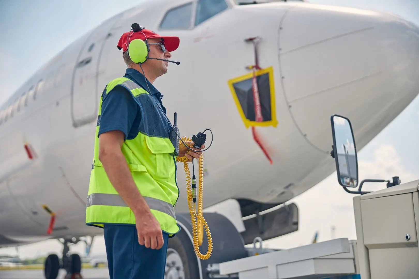 Agent de piste aéroportuaire en gilet de sécurité et casque de communication devant un avion.