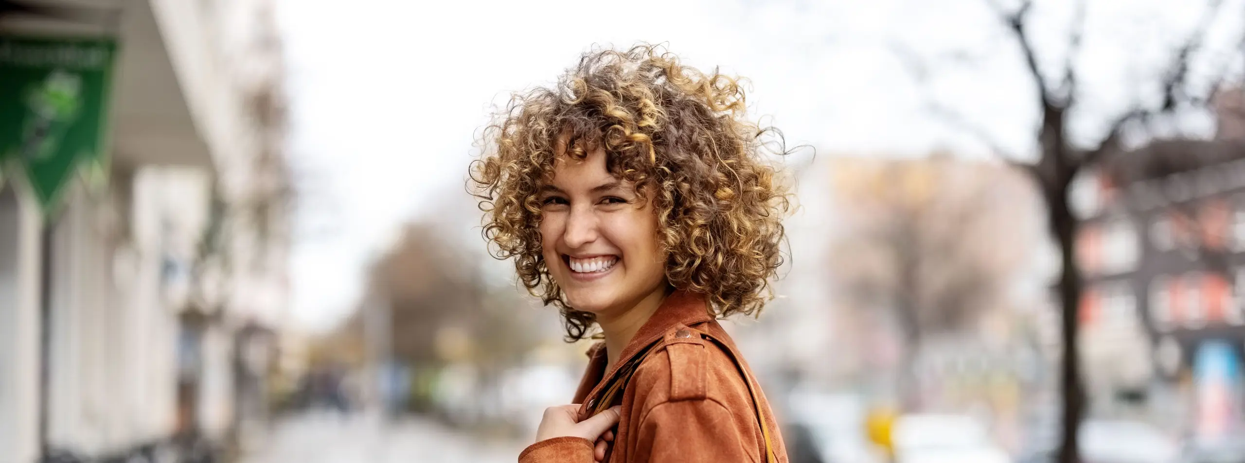 Une jeune femme souriante et dynamique marche en ville, prête pour de nouvelles opportunités professionnelles.