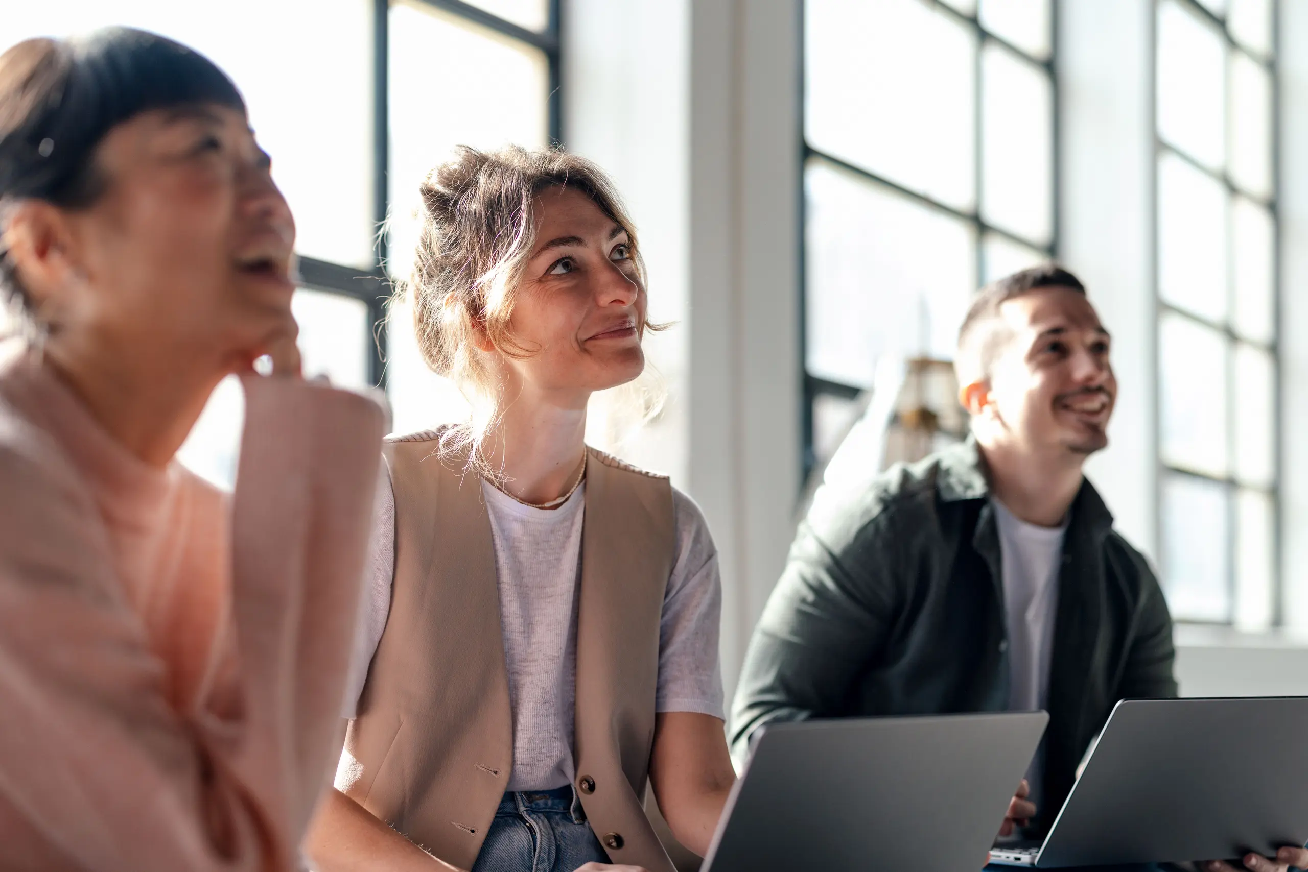 Trois collaborateurs souriants et attentifs lors d'une réunion de travail dans un bureau lumineux.