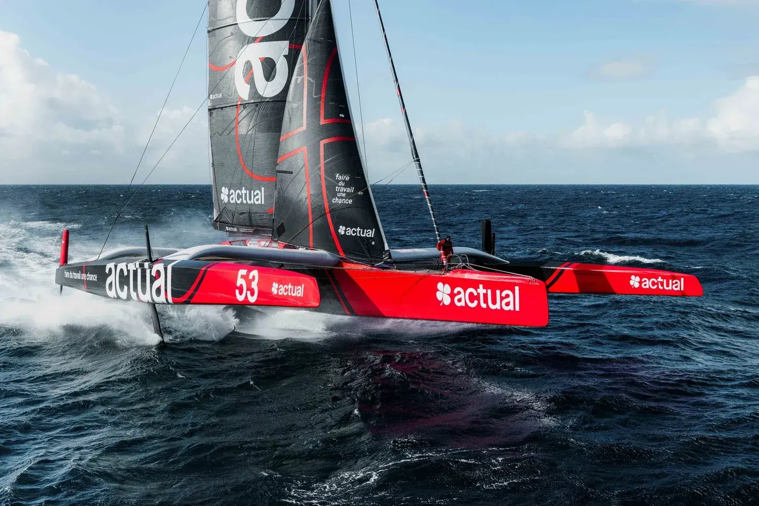 Trimaran de course rouge et noir du groupe Actual naviguant à grande vitesse sur l'océan.
