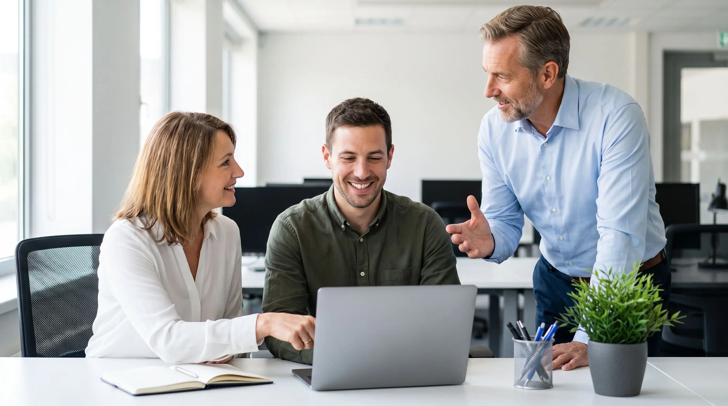 Trois collaborateurs échangent avec le sourire autour d'un ordinateur portable lors d'une intégration.