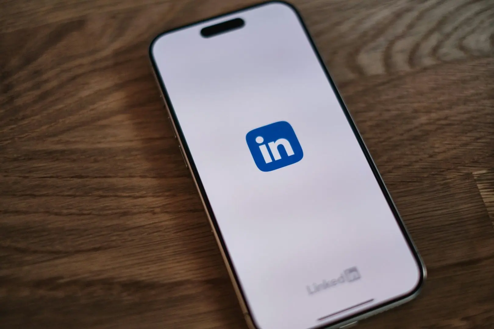 Un smartphone posé sur un bureau en bois affiche le logo du réseau professionnel LinkedIn.