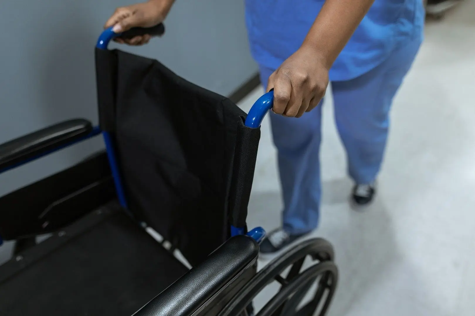 Un professionnel de santé en blouse bleue pousse un fauteuil roulant.