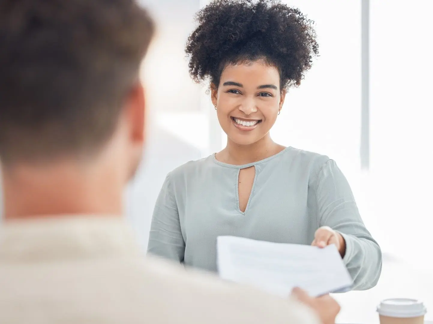 Une candidate souriante remet son CV à un recruteur lors d'un entretien.