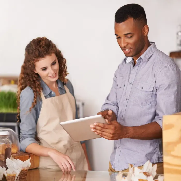 Un homme montre une tablette tactile à une employée portant un tablier dans un commerce.