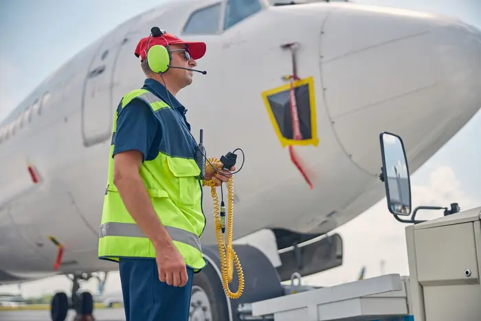 Agent de piste aéroportuaire en gilet de sécurité et casque de communication devant un avion.
