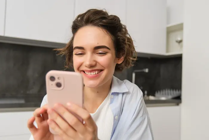 Une jeune femme souriante gère son épargne sur son smartphone.