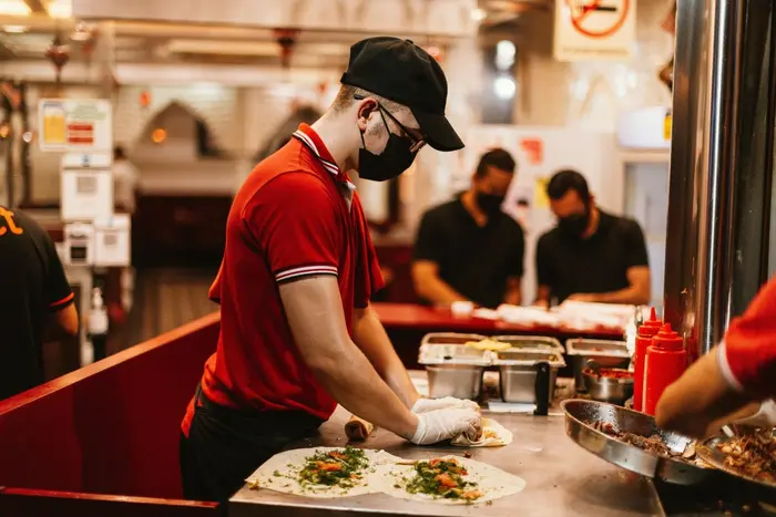 Un jeune équipier en restauration rapide prépare des wraps en cuisine lors d'un job étudiant.