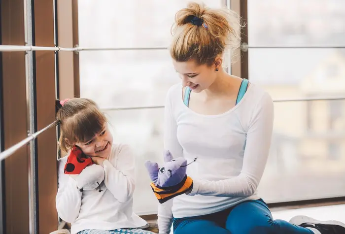 Une éducatrice spécialisée échange avec une enfant en jouant avec des marionnettes.