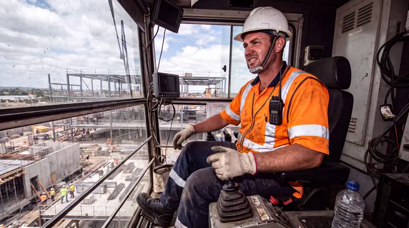 Grutier professionnel en cabine, équipé d'un casque et d'un gilet de sécurité, pilotant sa grue sur un chantier.
