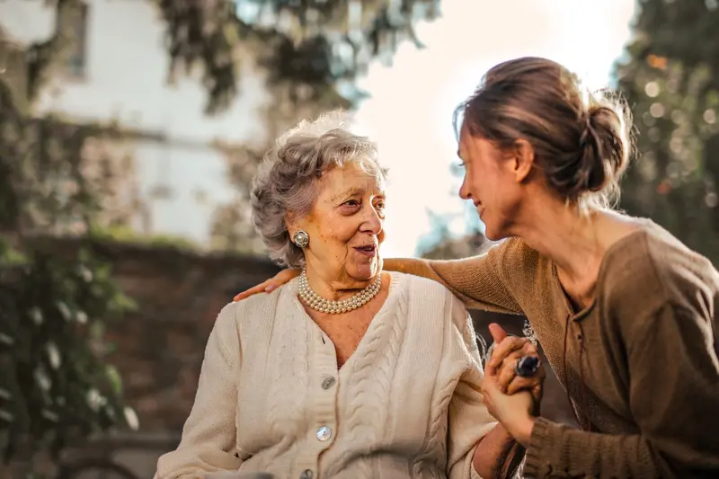 Une auxiliaire de vie échange un regard bienveillant avec une personne âgée tout en lui tenant la main.