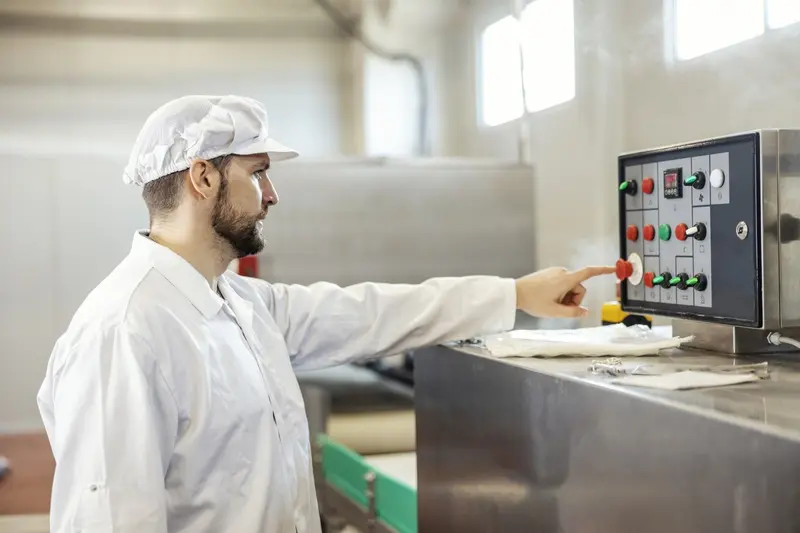 Un ouvrier agroalimentaire en tenue d'hygiène utilise le panneau de commande d'une machine de production.
